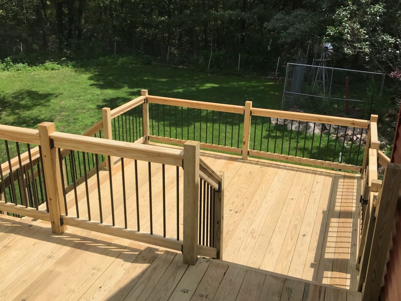 Wooden deck with black railing and steps leading to yard.