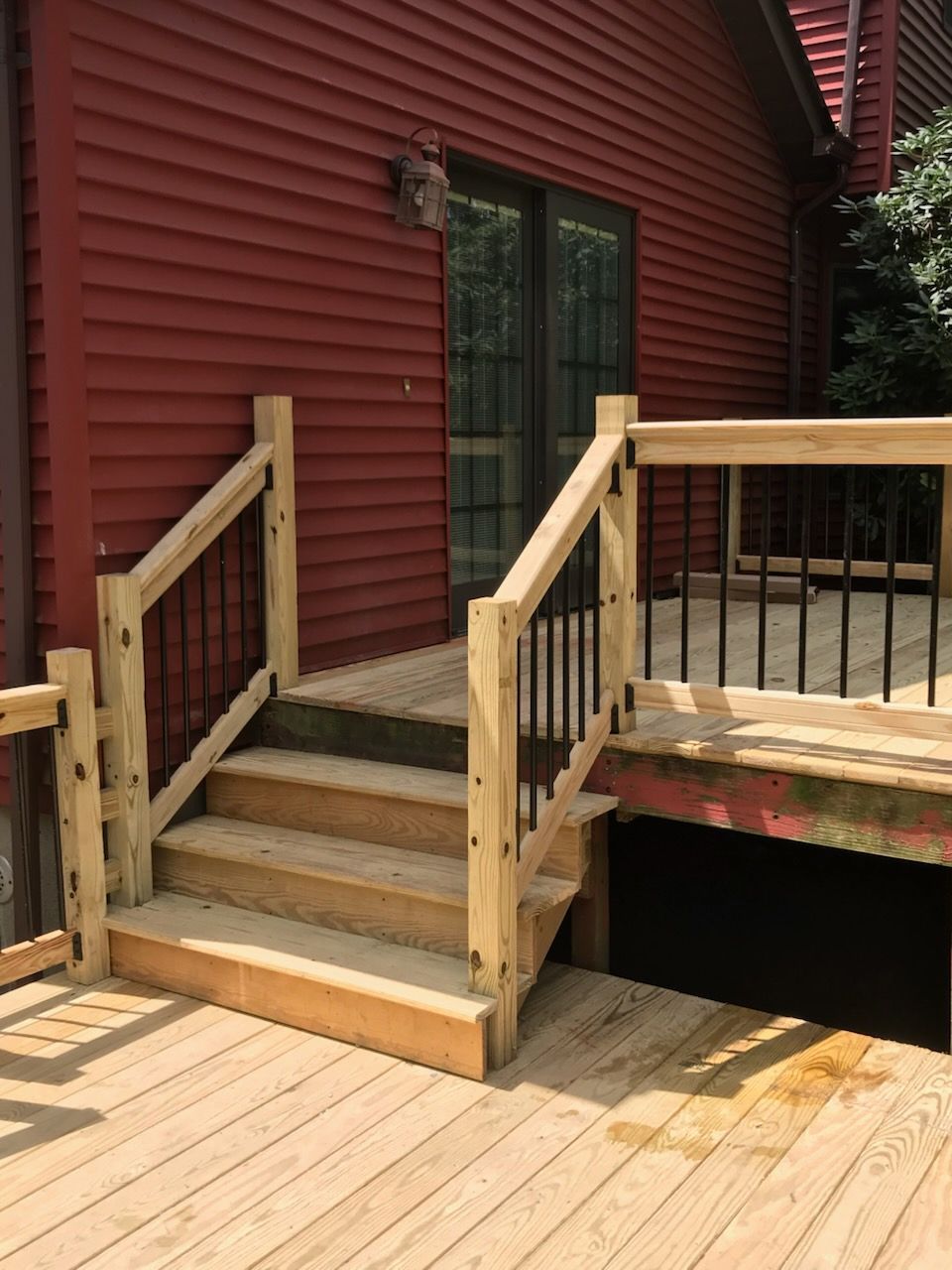 Wooden deck with stairs leading to a red house with a sliding glass door. 