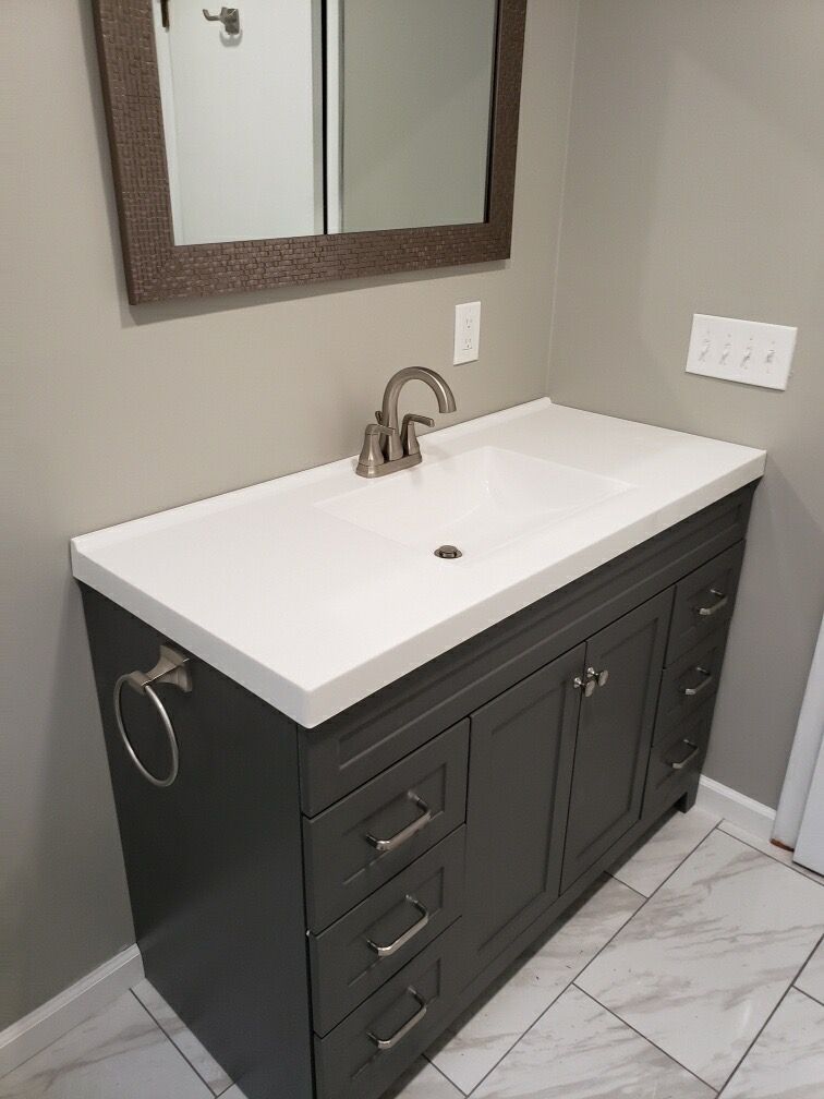 Dark gray bathroom vanity with white countertop, faucet, and mirror.