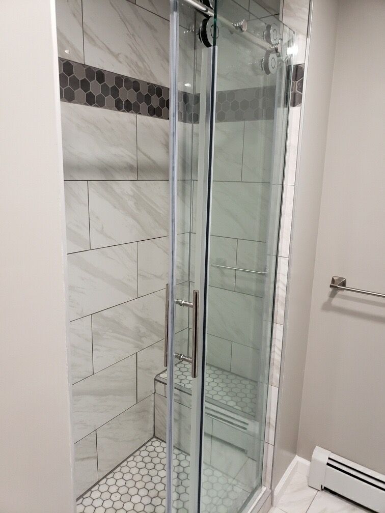 Modern shower with glass door and marble tile. Includes a built-in bench.