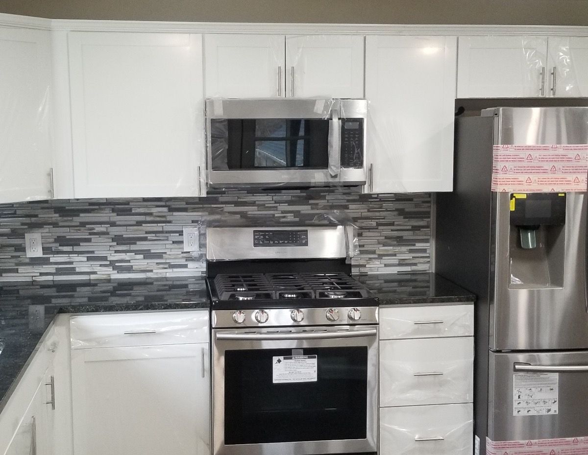 Kitchen with white cabinets, stainless steel appliances, dark countertop, and mosaic backsplash.