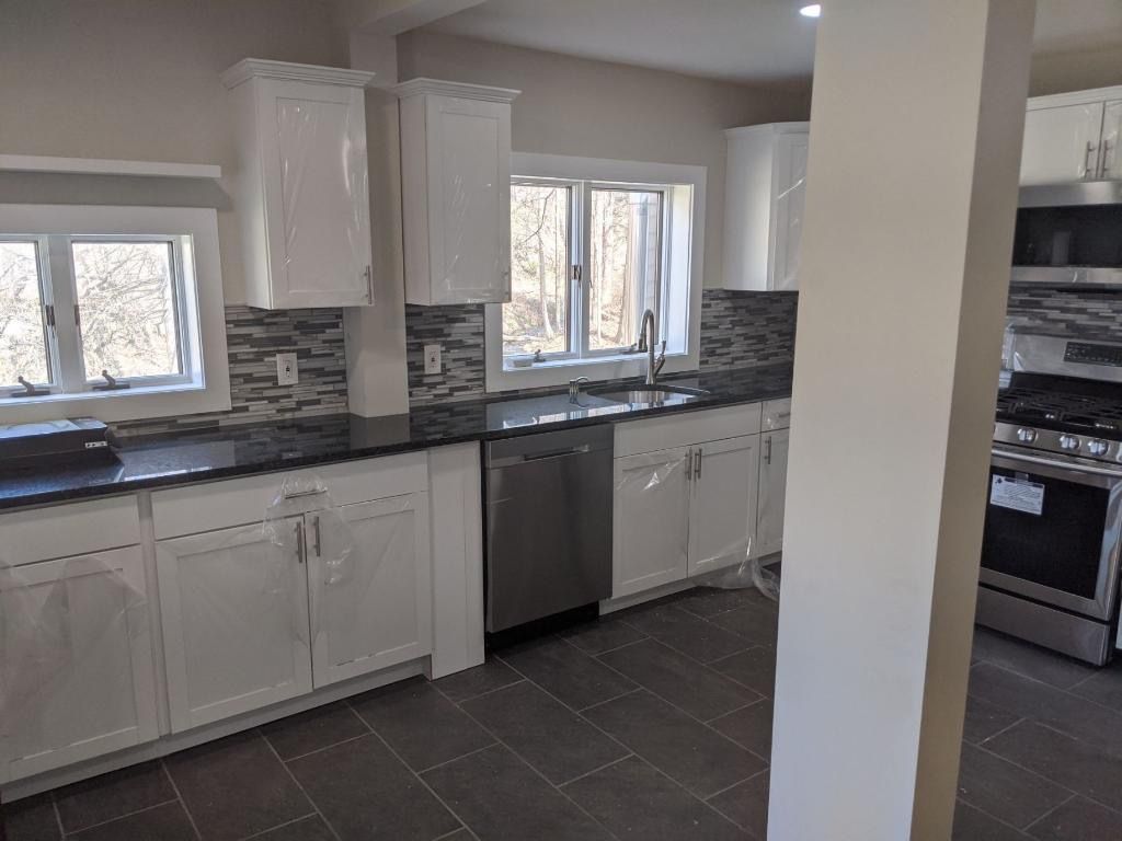 White kitchen with dark countertops, stainless steel appliances, tile backsplash, and two windows.