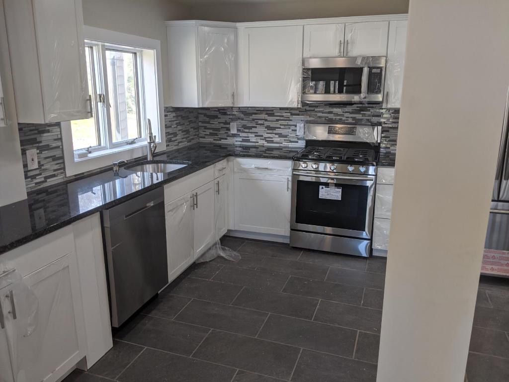 Newly renovated kitchen with white cabinets, stainless steel appliances, and dark countertops.