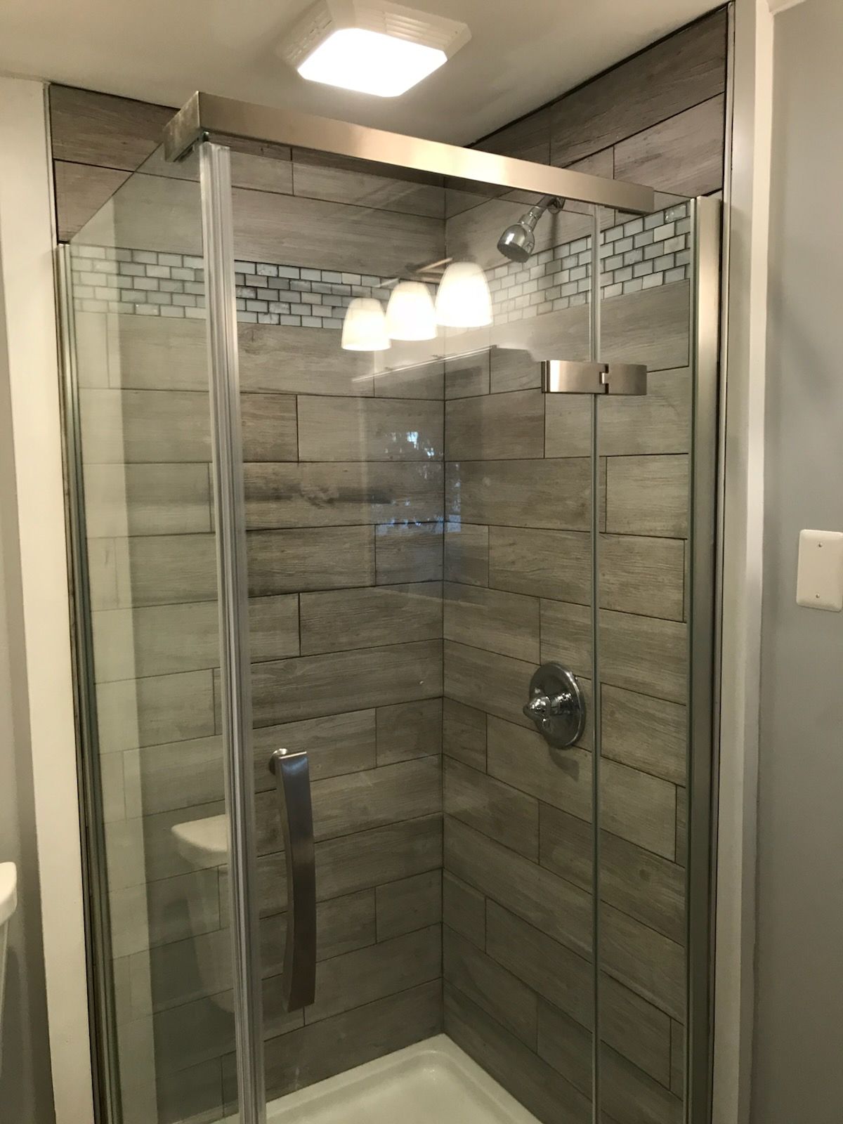 Shower with glass doors, gray and blue tiled walls, and silver fixtures.