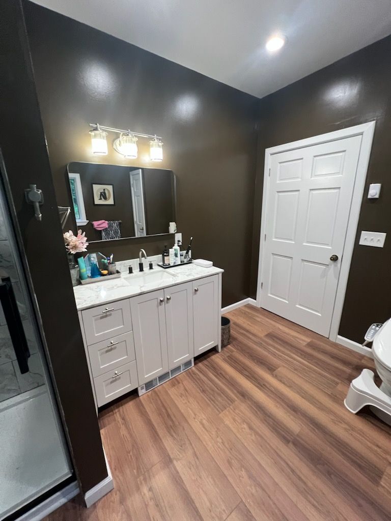 Bathroom with white vanity, brown walls, and wood-look flooring. White door on right.
