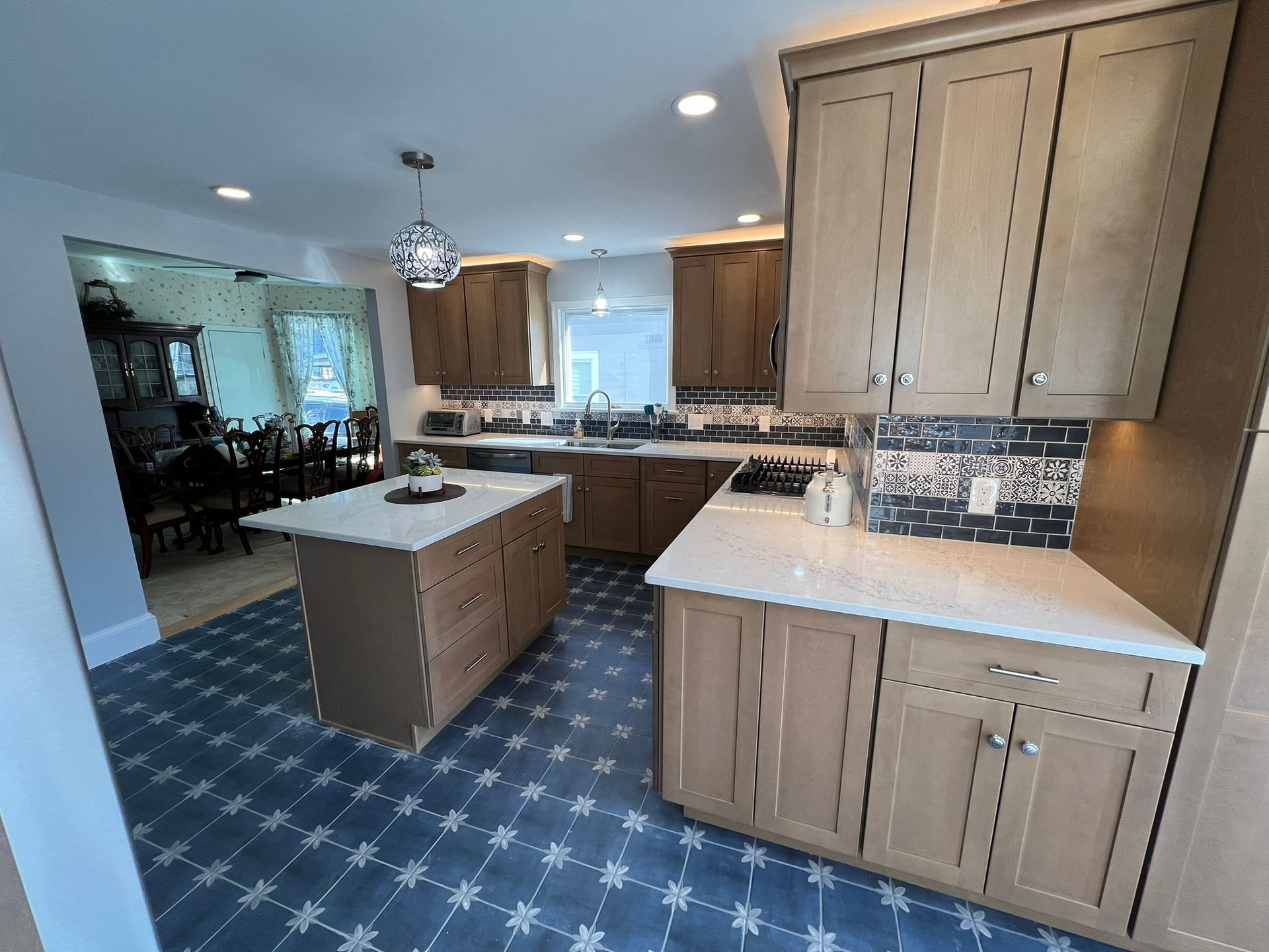 Kitchen with light wood cabinets, white countertops, and blue patterned tile flooring.