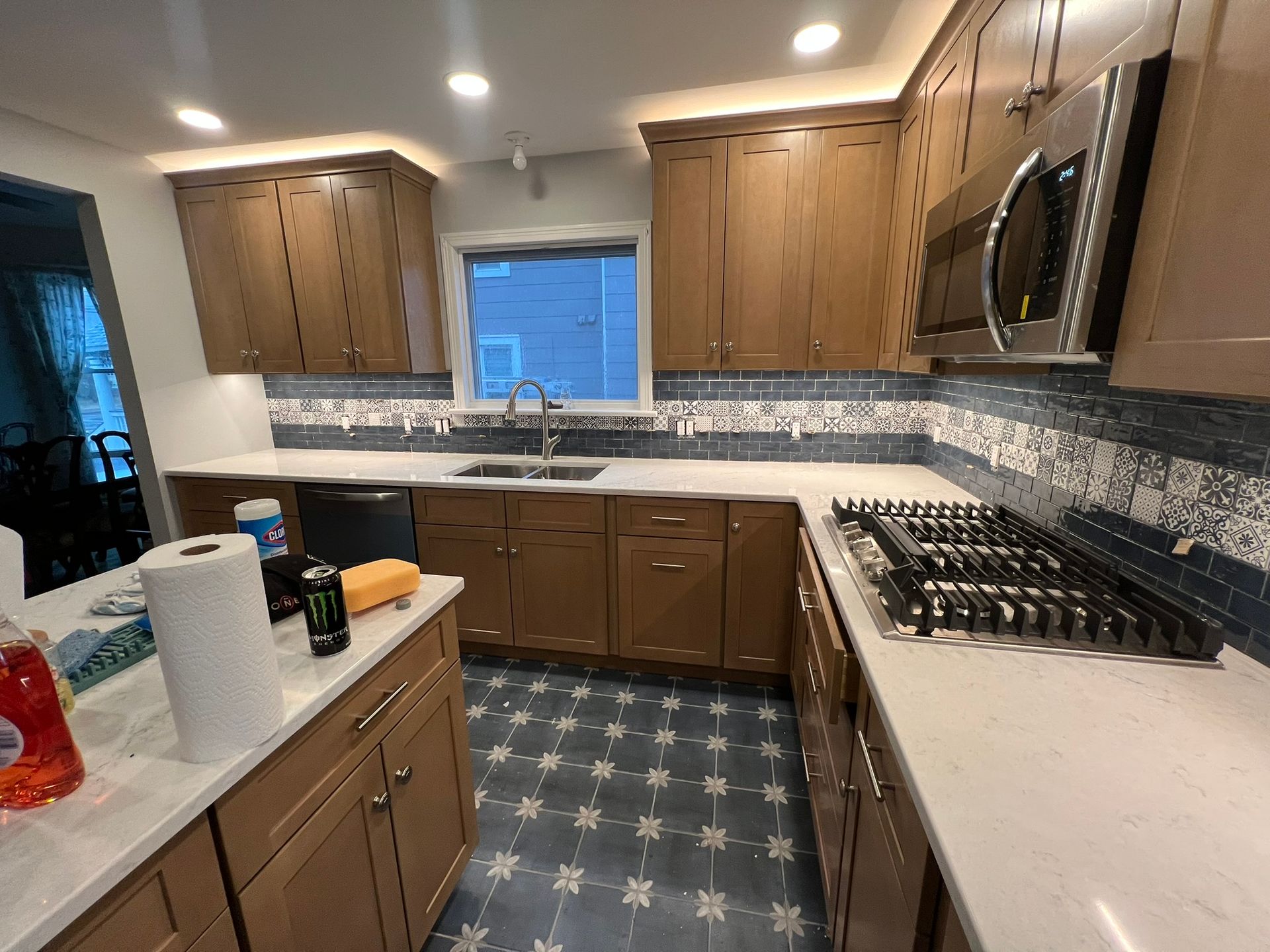 Kitchen with brown cabinets, white countertops, blue backsplash, stainless steel appliances, and patterned floor.