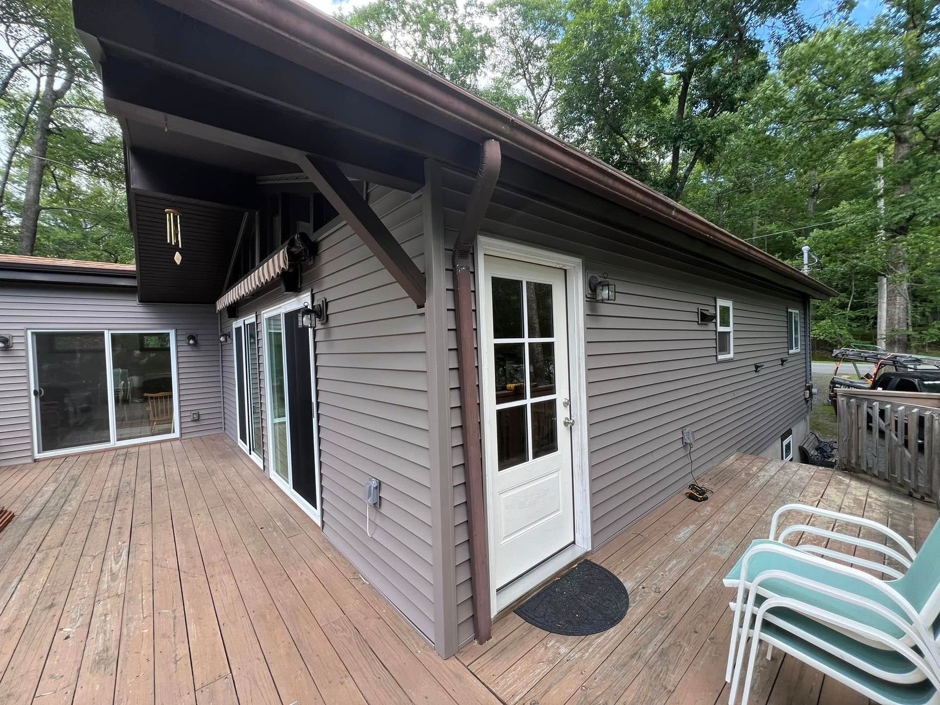 Exterior of a house with a wooden deck. Gray siding, white door, and sliding glass doors.