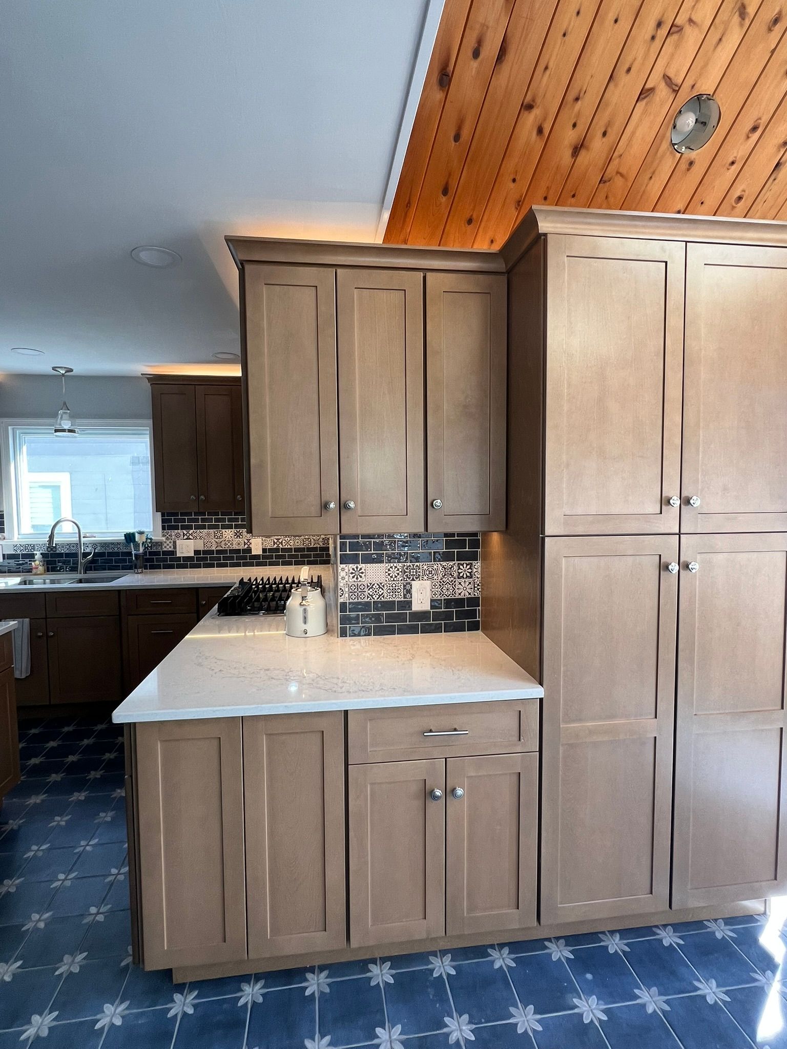 Kitchen with light wood cabinets, white countertops, and blue patterned floor.
