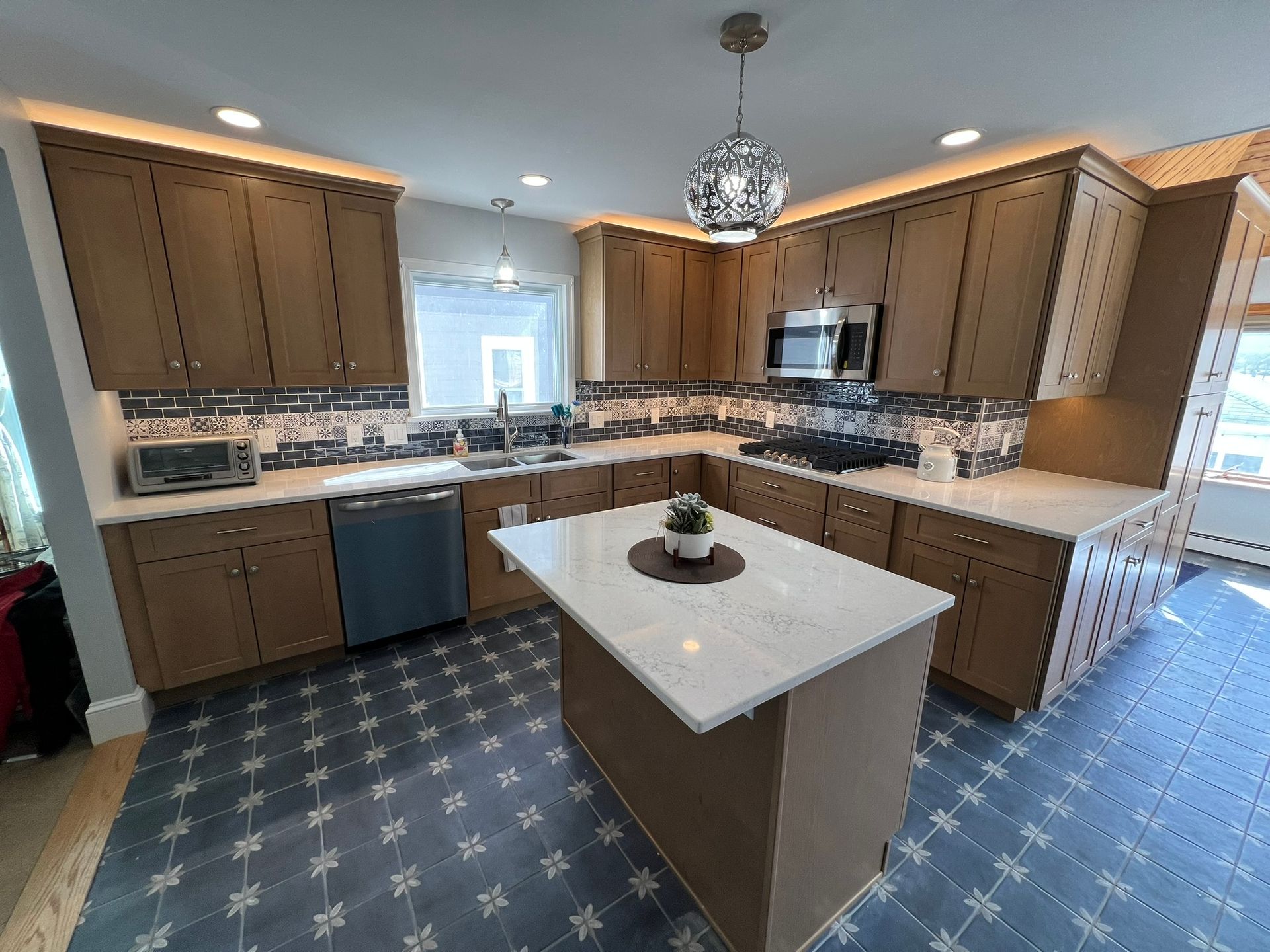 Modern kitchen with brown cabinets, white countertops, and blue patterned tile floor.