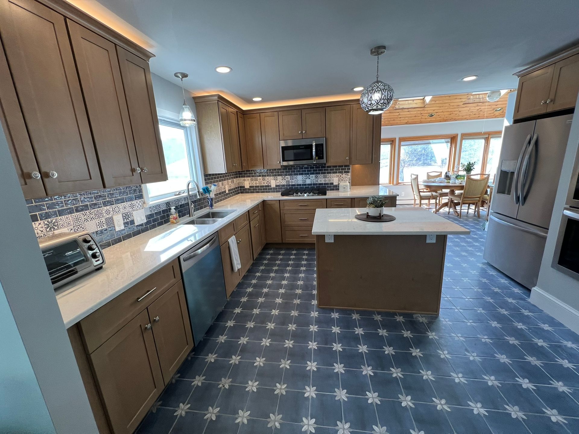 U-shaped kitchen with light wood cabinets, stainless steel appliances, and blue patterned tile floor.