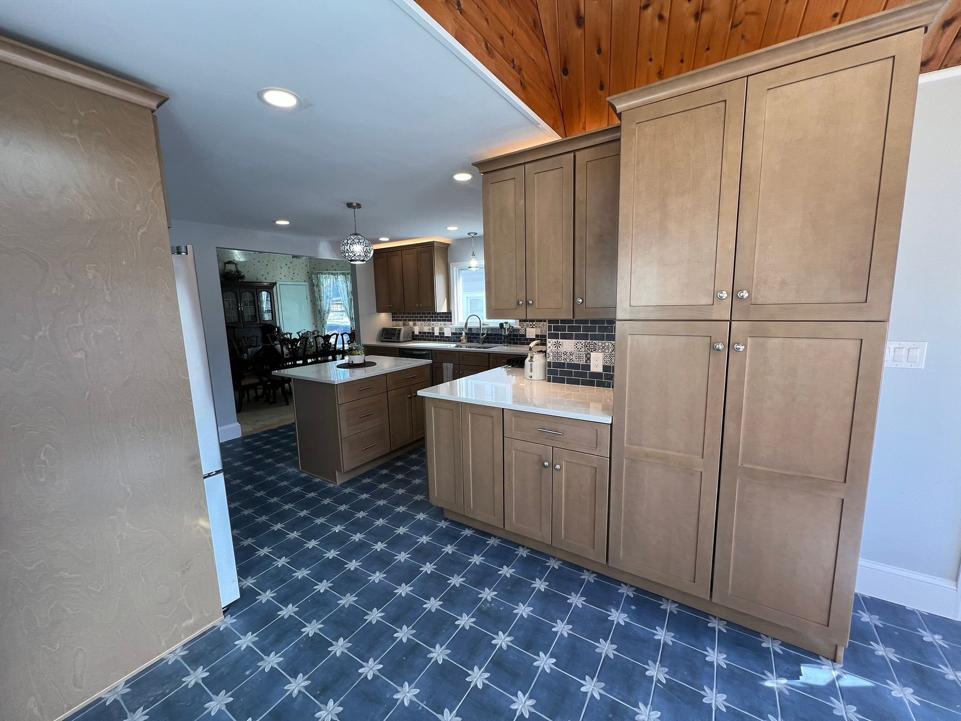Kitchen with tan cabinets, blue tile floor, island, and wood ceiling.