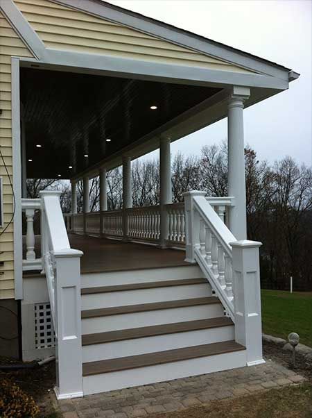 Covered porch with white columns, stairs, and railing; light brown deck.