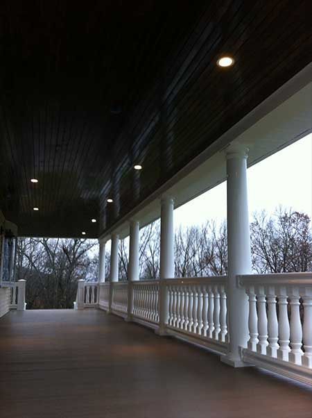 Covered porch with white columns, railings, and dark wood ceiling.