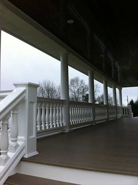 White porch with columns and balustrade, wooden flooring, overcast sky.