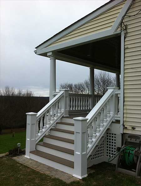 White porch with steps leading to a covered entrance of a beige house on an overcast day.