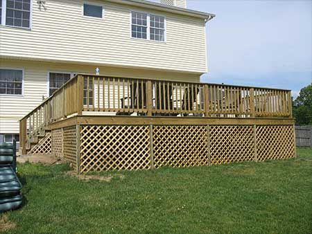 Wooden deck attached to a two-story beige house with lattice skirting.