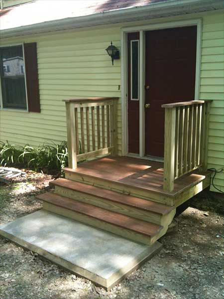 Wooden porch with steps leading to a burgundy door on a yellow house.