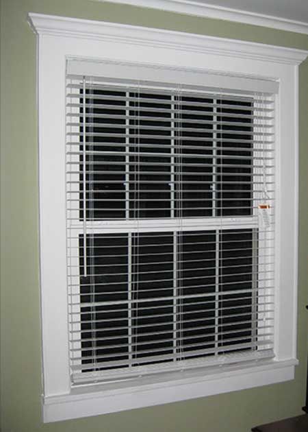White-framed window with blinds closed, set against a light green wall.