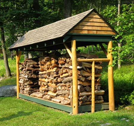 Wood-filled shed with angled roof in grassy area, supported by wooden beams.