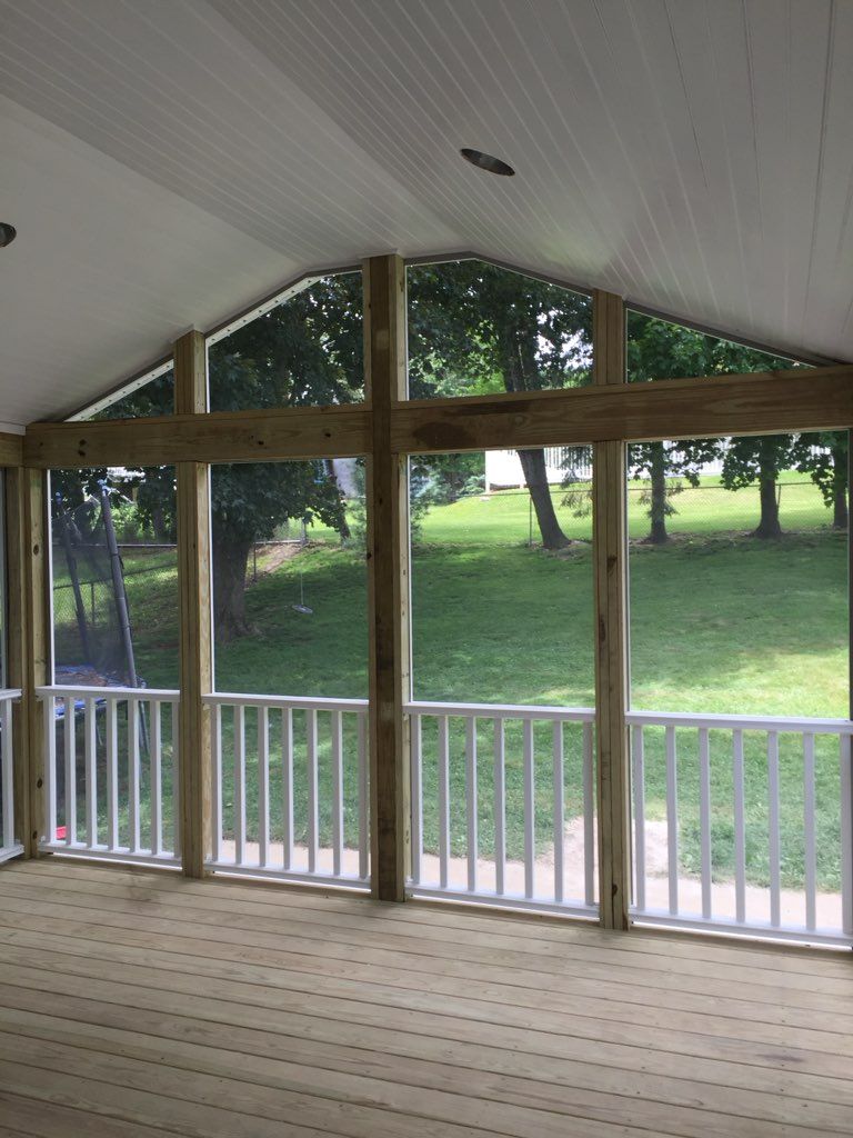 Screened-in porch with wood frame and white railing, looking out onto a grassy yard with trees.