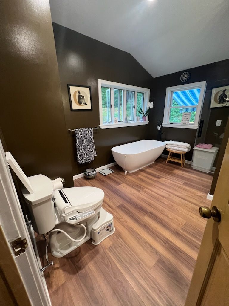 Bathroom with brown walls, wooden floor, toilet with bidet seat, and a freestanding tub.