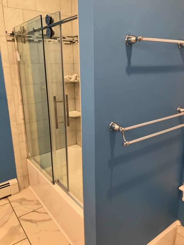 Bathroom with a glass shower, blue wall, and chrome towel racks.