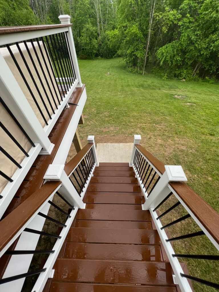 Two-story wooden deck and stairs with brown railings and a white double door entrance.