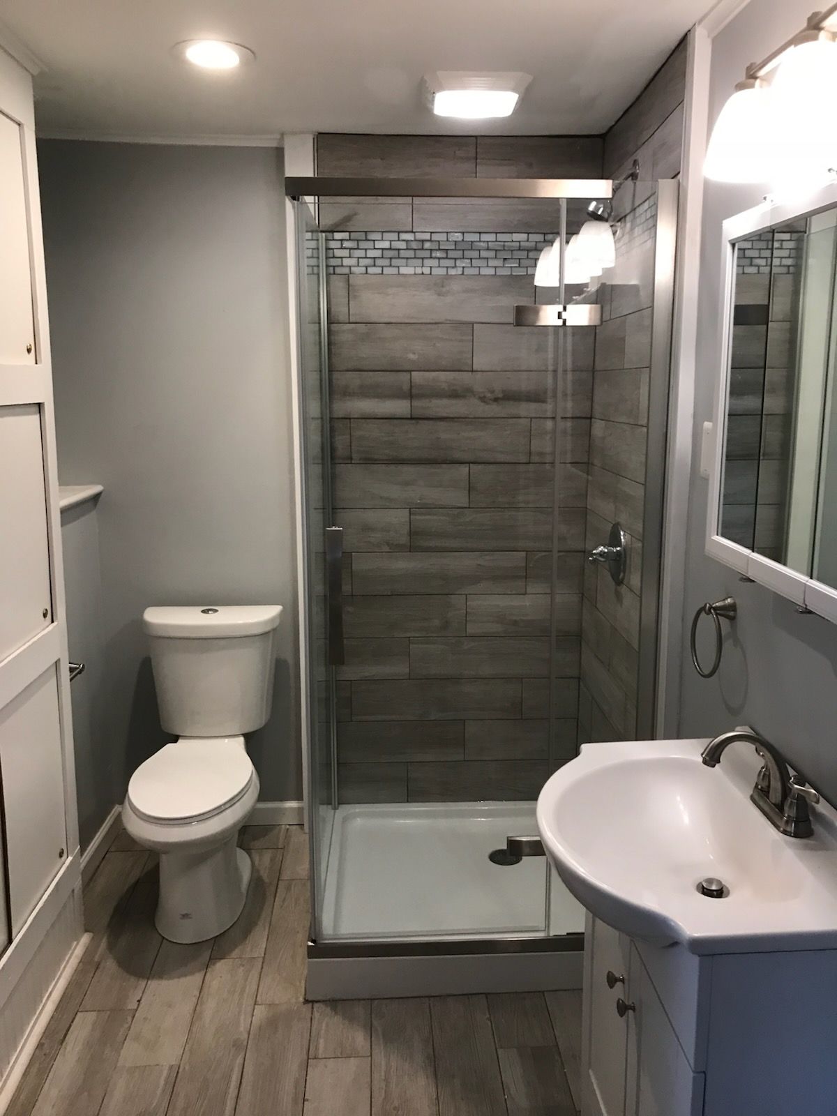 Small bathroom with gray walls, tiled shower, toilet, and vanity with a sink.
