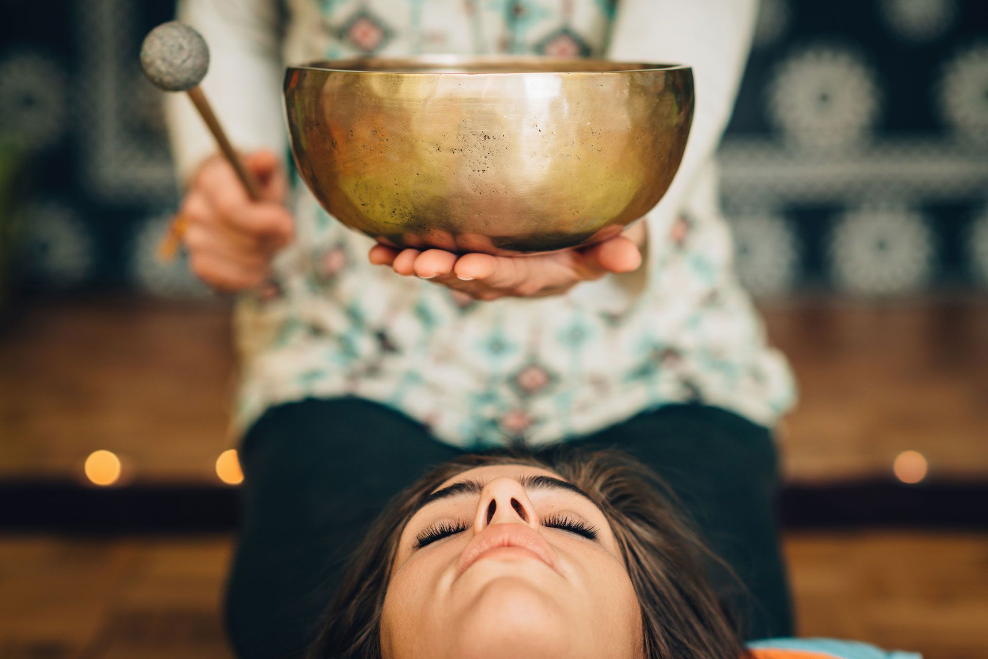 Person receiving sound bowl therapy; bowl held above face, indoor setting.