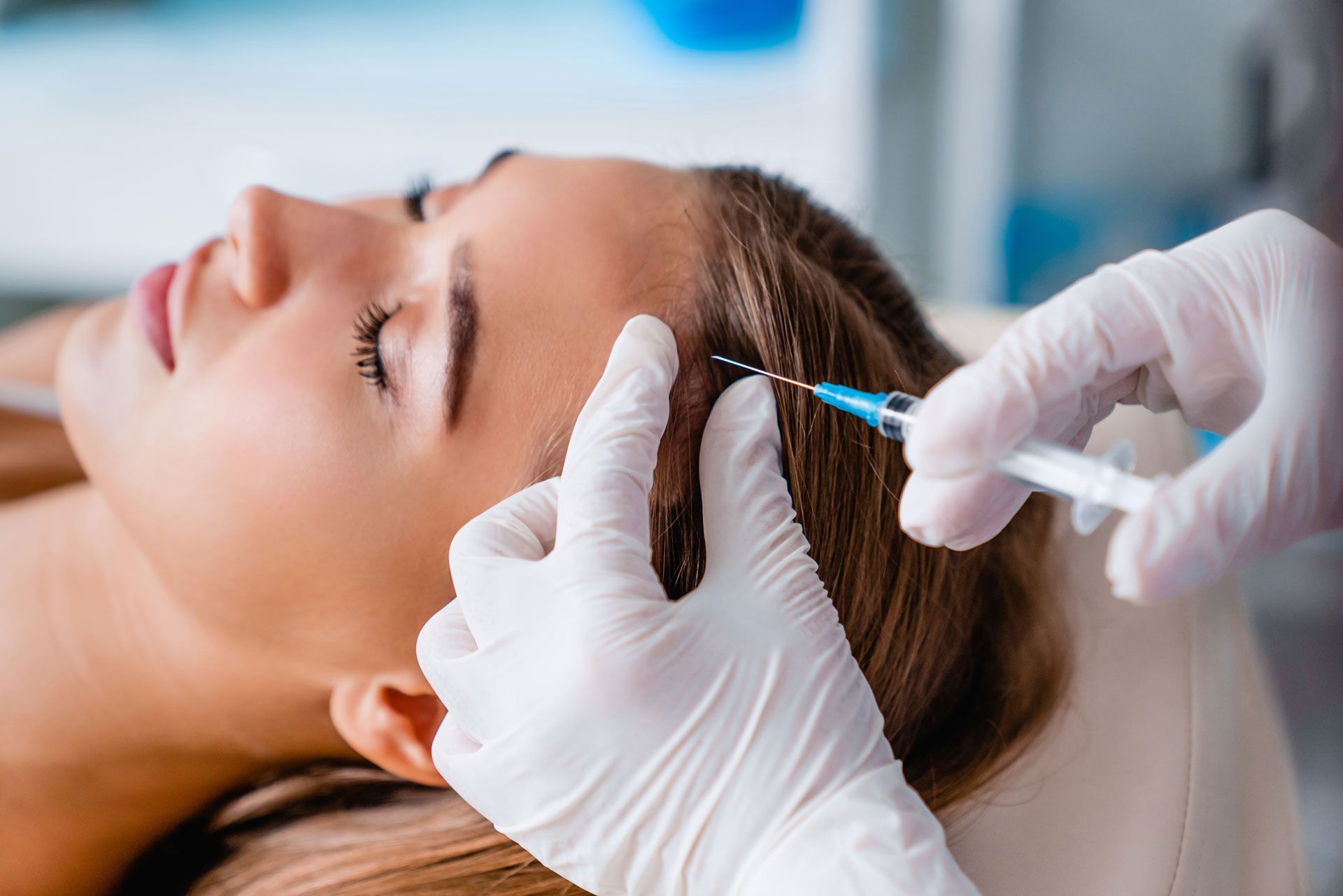 Person receiving an injection in their scalp by a gloved hand, indoors.