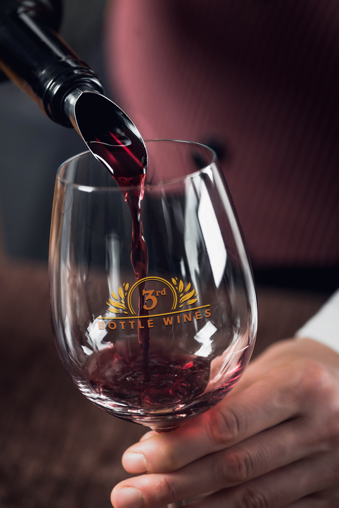 Red wine being poured into a glass with a logo, held by a person in a formal setting.