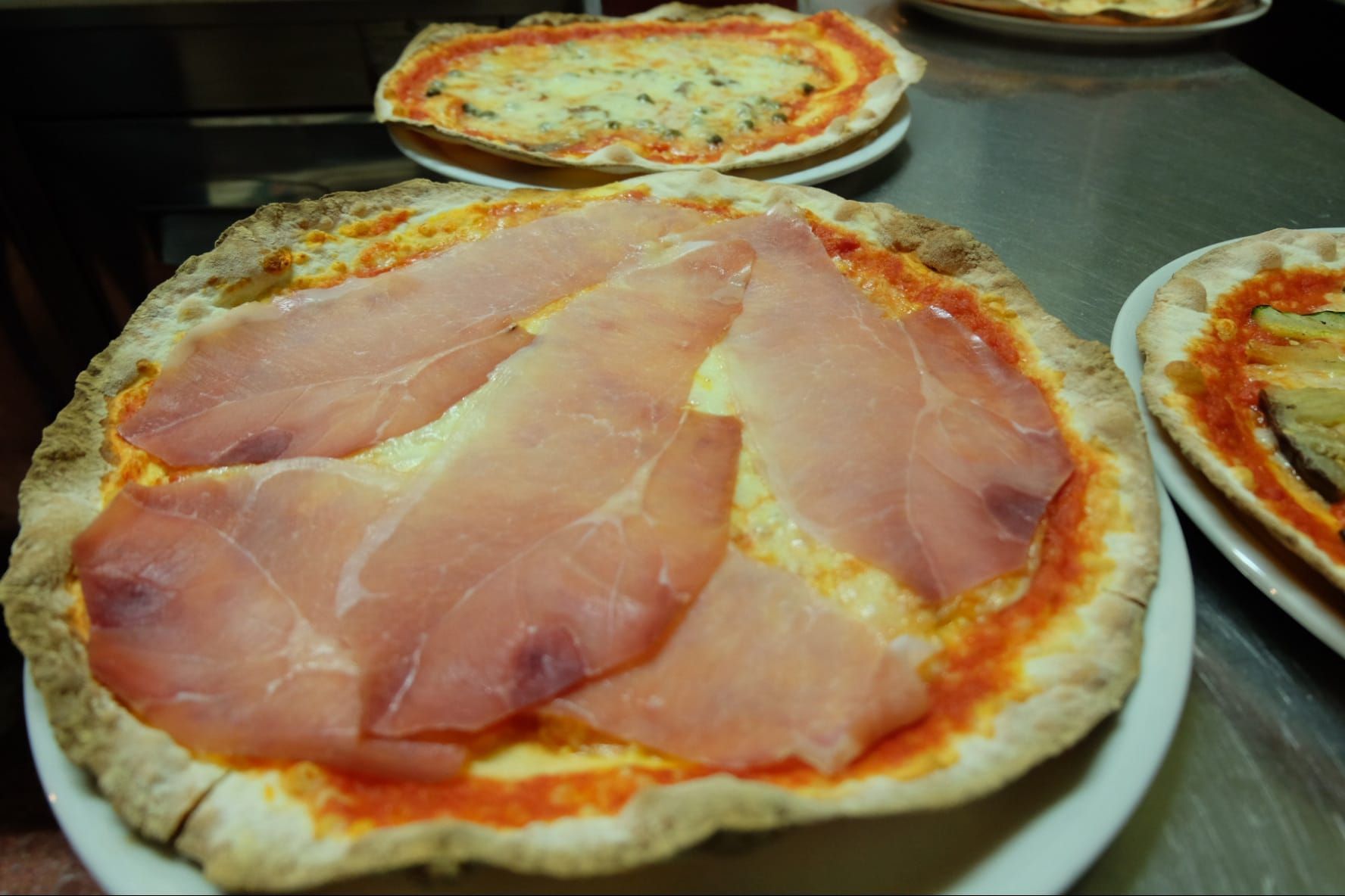 un primo piano di una pizza con prosciutto su un piatto