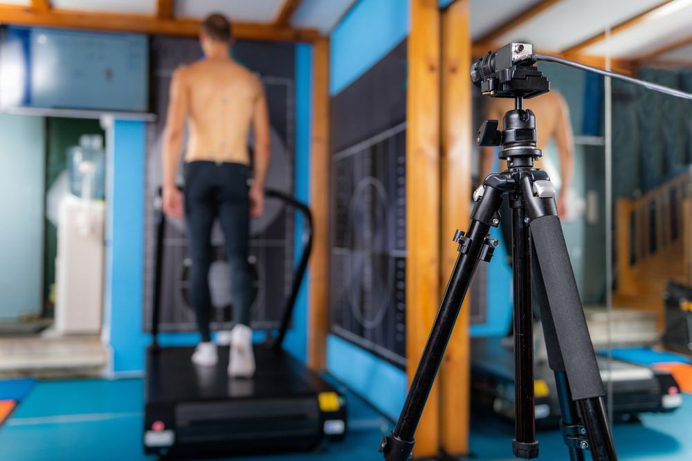 A Man Is Standing On A Treadmill Next To A Camera On A Tripod — Sandy Gugenberger Podiatrist in Port Macquarie, NSW