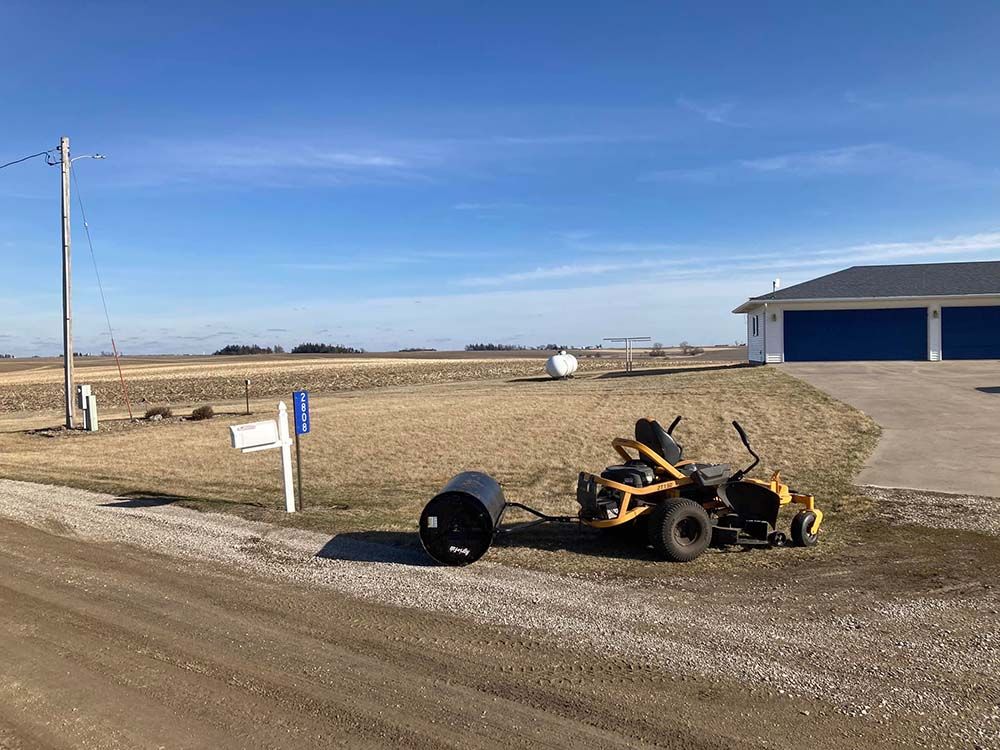 A yellow lawn mower is parked on the side of a dirt road.