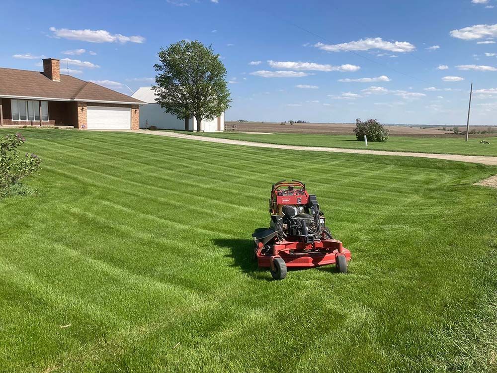 A red lawn mower is cutting a lush green lawn in front of a house.