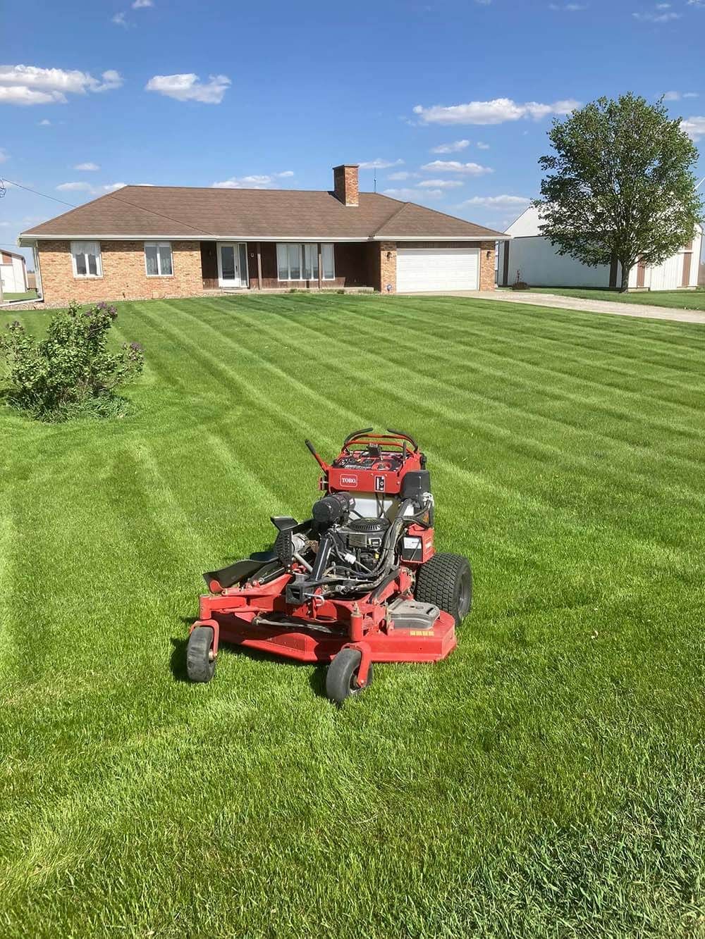 A red lawn mower is sitting on top of a lush green lawn in front of a house.