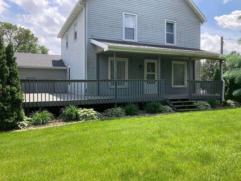 A white house with a large porch and a large lawn in front of it.