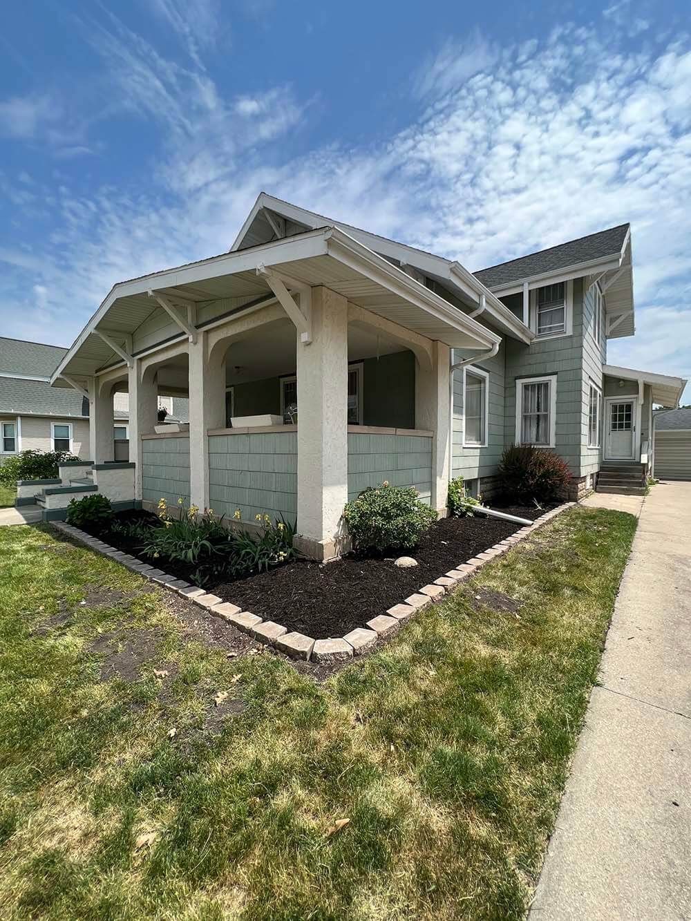 A house with a porch and a sidewalk in front of it.