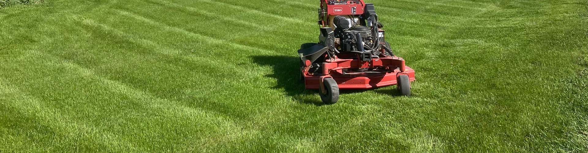 A red lawn mower is cutting a lush green lawn.
