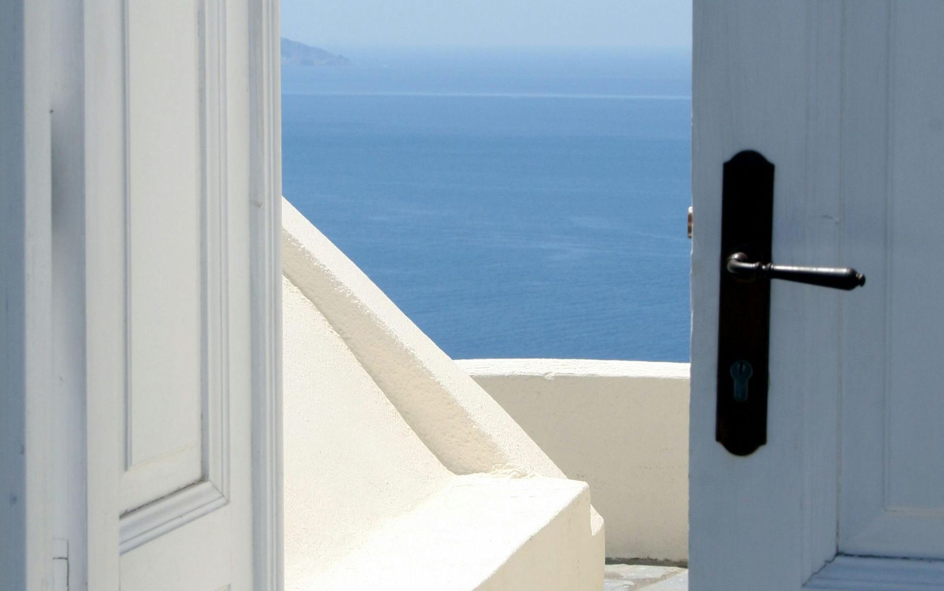 A white door with a black handle is open to a view of the ocean.