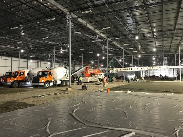 A large warehouse under construction with trucks and a crane.