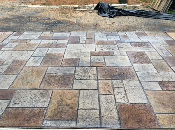 A concrete driveway with a brick pattern and a black tarp on the ground.