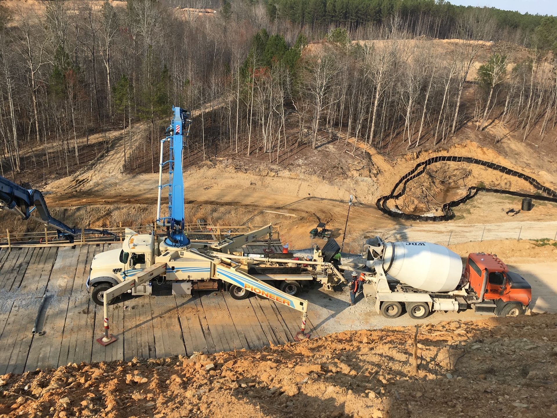 A concrete mixer truck is driving down a dirt road next to a concrete pump.