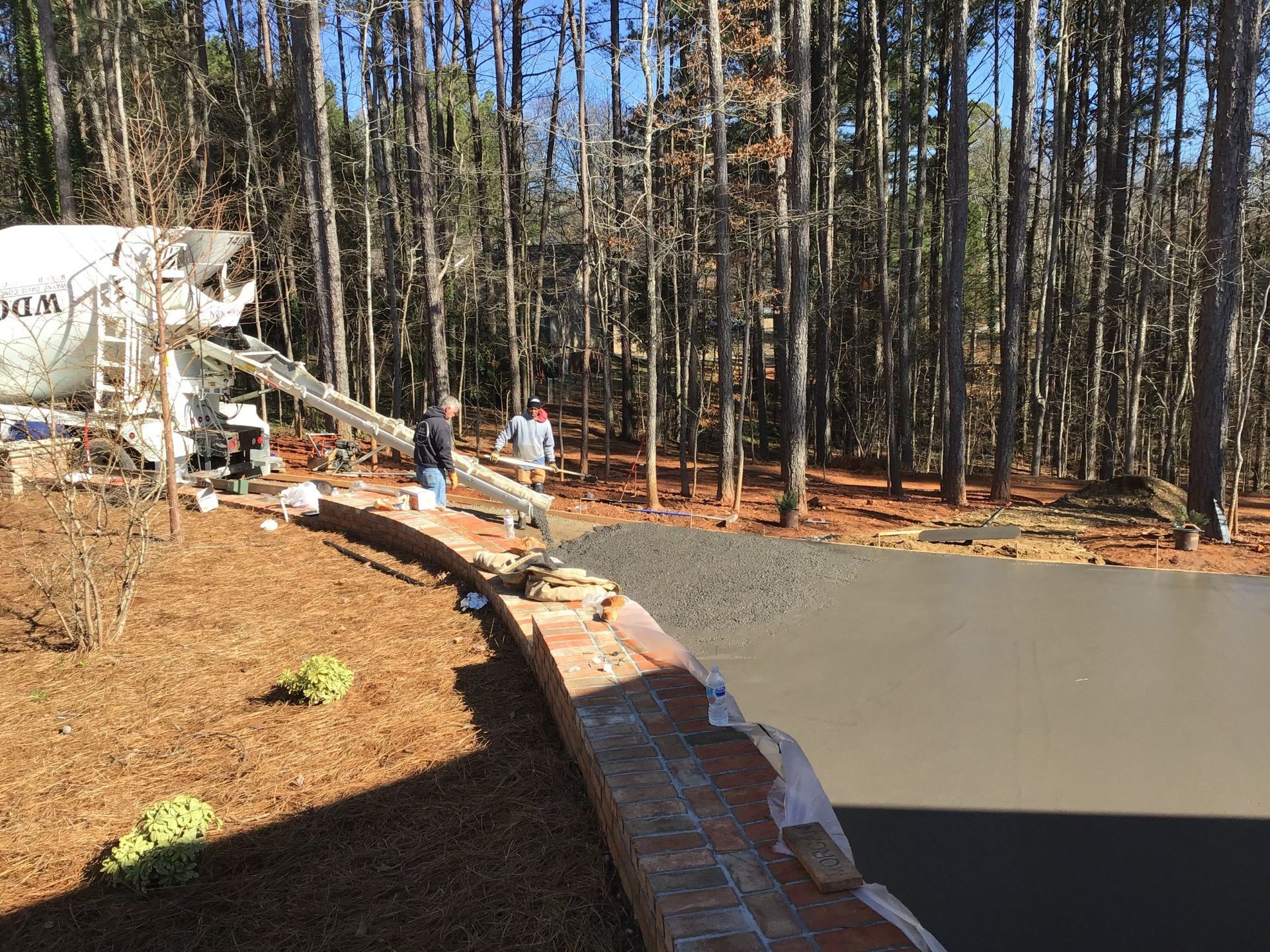 A concrete truck is pouring concrete into a driveway in the woods.