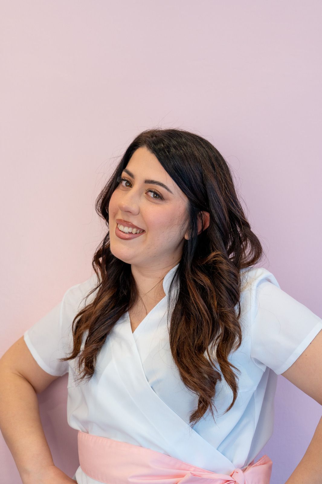 Una donna che indossa una camicia bianca e una cintura rosa è in piedi davanti a un muro rosa.