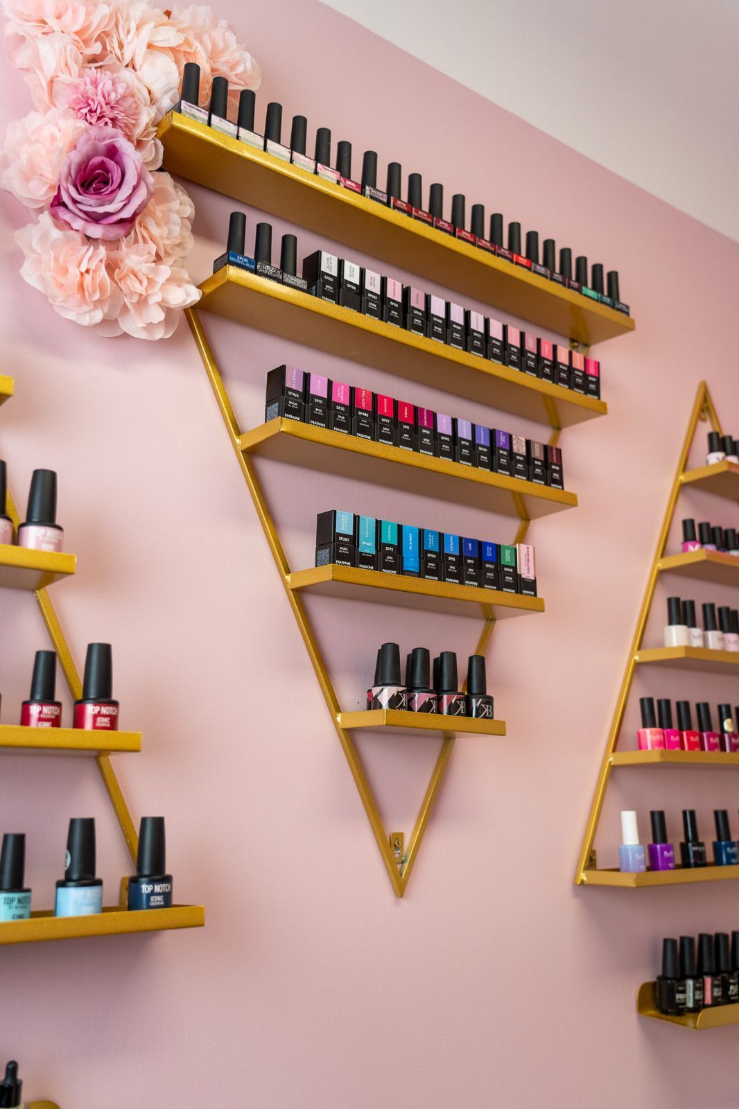 Un salone per unghie con scaffali pieni di smalti e fiori alle pareti.