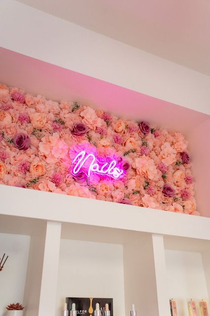 Un'insegna al neon è posta sopra una parete di fiori rosa.