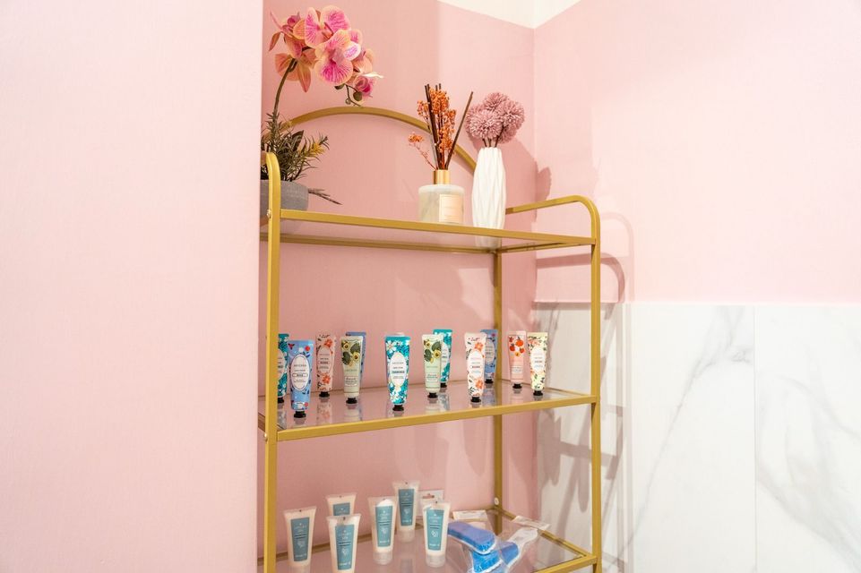 Uno scaffale pieno di bottiglie di lozione e fiori su una parete rosa.