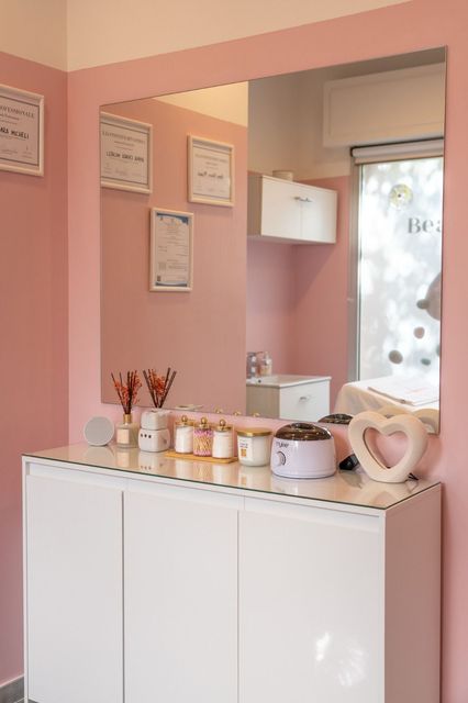 Una stanza rosa con uno specchio e una cassettiera con sopra delle candele.